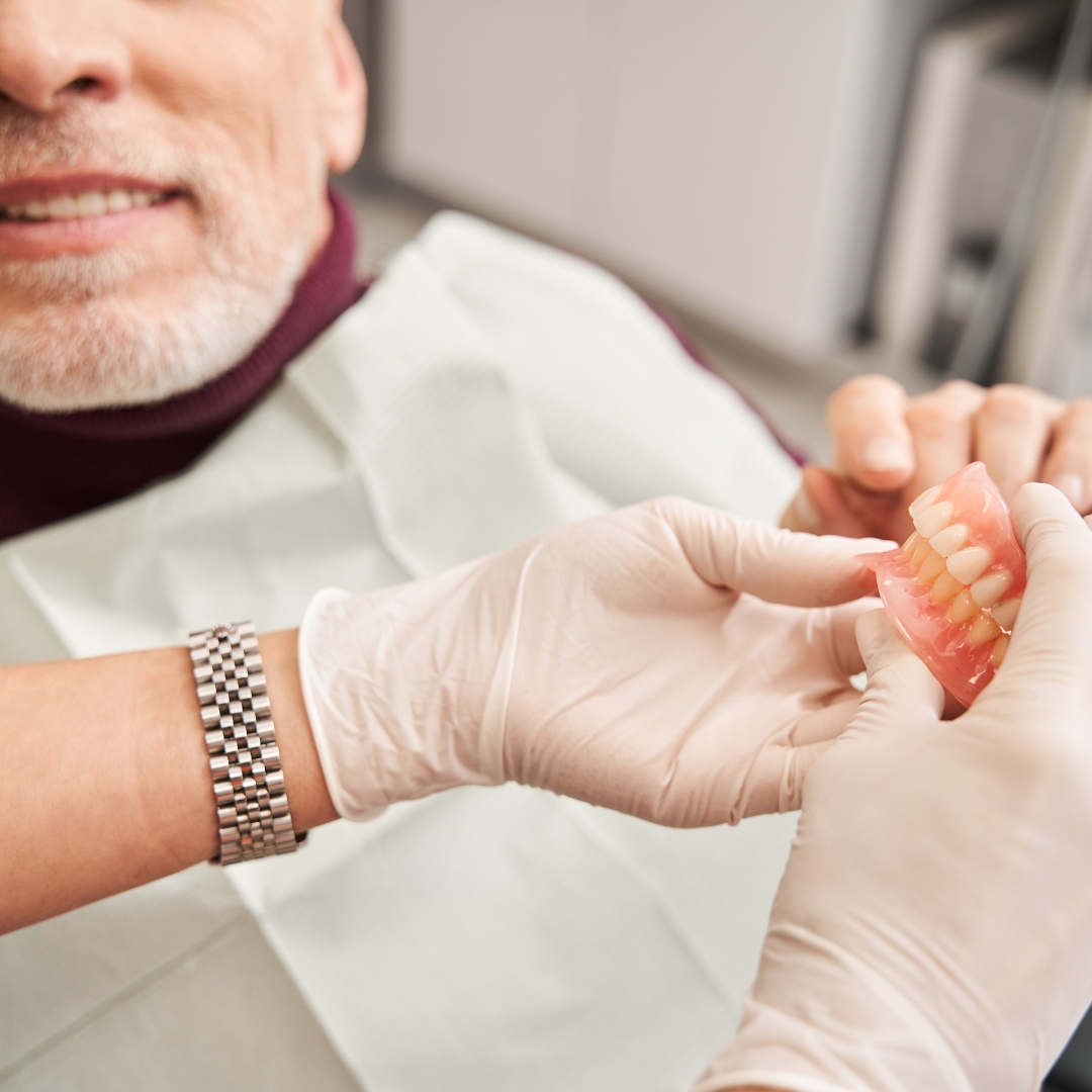 Dentist showing to senior grey haired patient teeth dentures while working at the prosthodontics dental clinic.