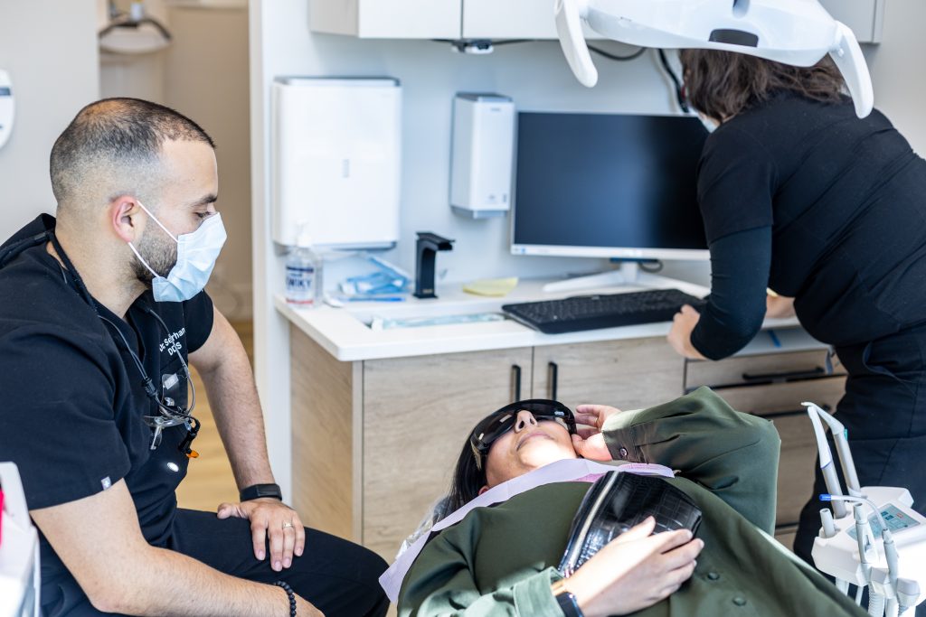 A woman sitting in a dentist's chair, talking to a dentist. Contact us today to book an appointment.