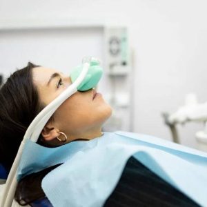 Patient tilting back in dental chair receiving nasal sedation mask from dentist's hands in clinical office